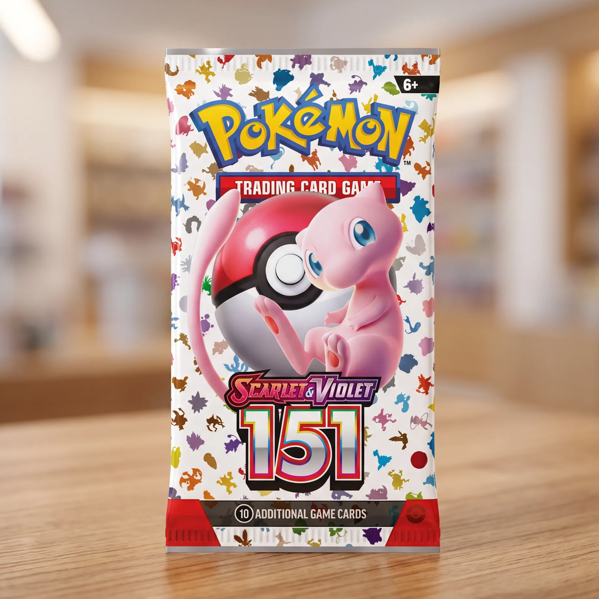 A Pokémon Scarlet & Violet 151 trading card booster pack standing upright on a wooden table with a blurred indoor background.